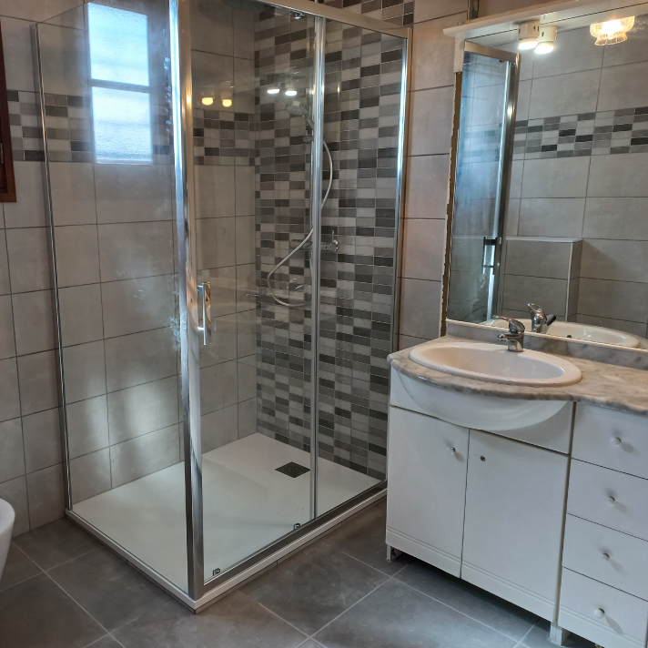 Salle de bain modernisée après travaux avec cabine de douche vitrée et meuble vasque installée par un plombier LIMA à Dax, dans les Landes.